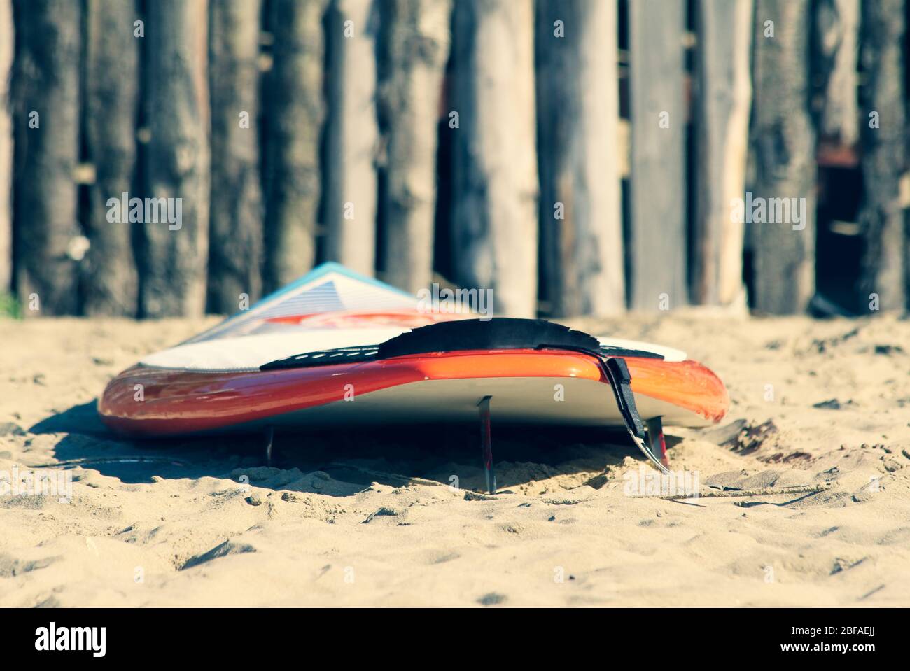 Gros plan sur un surf branché au lever du soleil ou au coucher du soleil sur la plage de sable. Clôture en bois sur le fond. Concept de vacances. Vacances d'été. Tourisme, s Banque D'Images