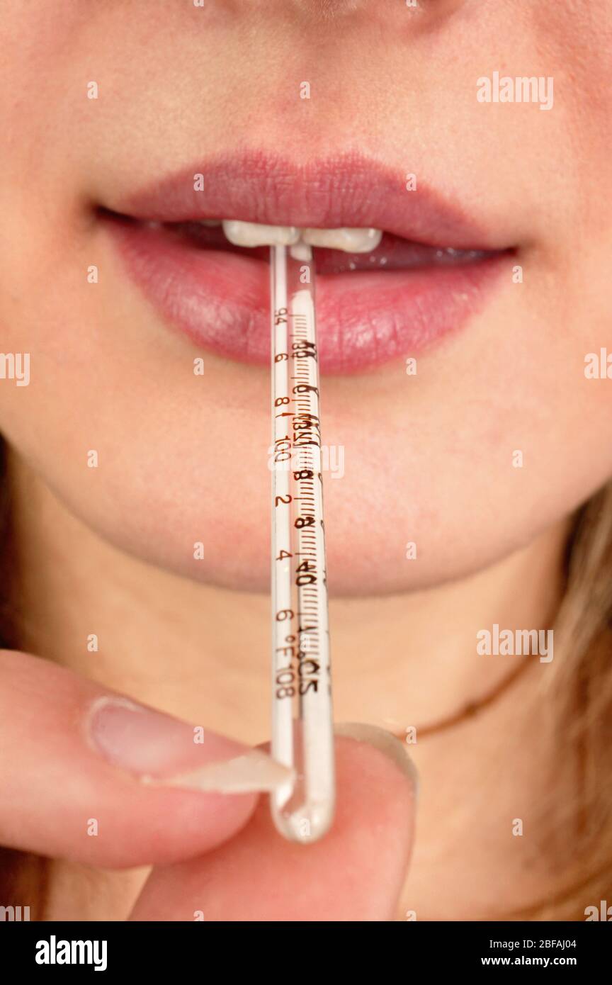 Une femme avec un thermomètre au mercure dans sa bouche. Elle prend sa  propre température pour diagnostiquer les symptômes de la grippe (grippe).  Elle utilise un Photo Stock - Alamy