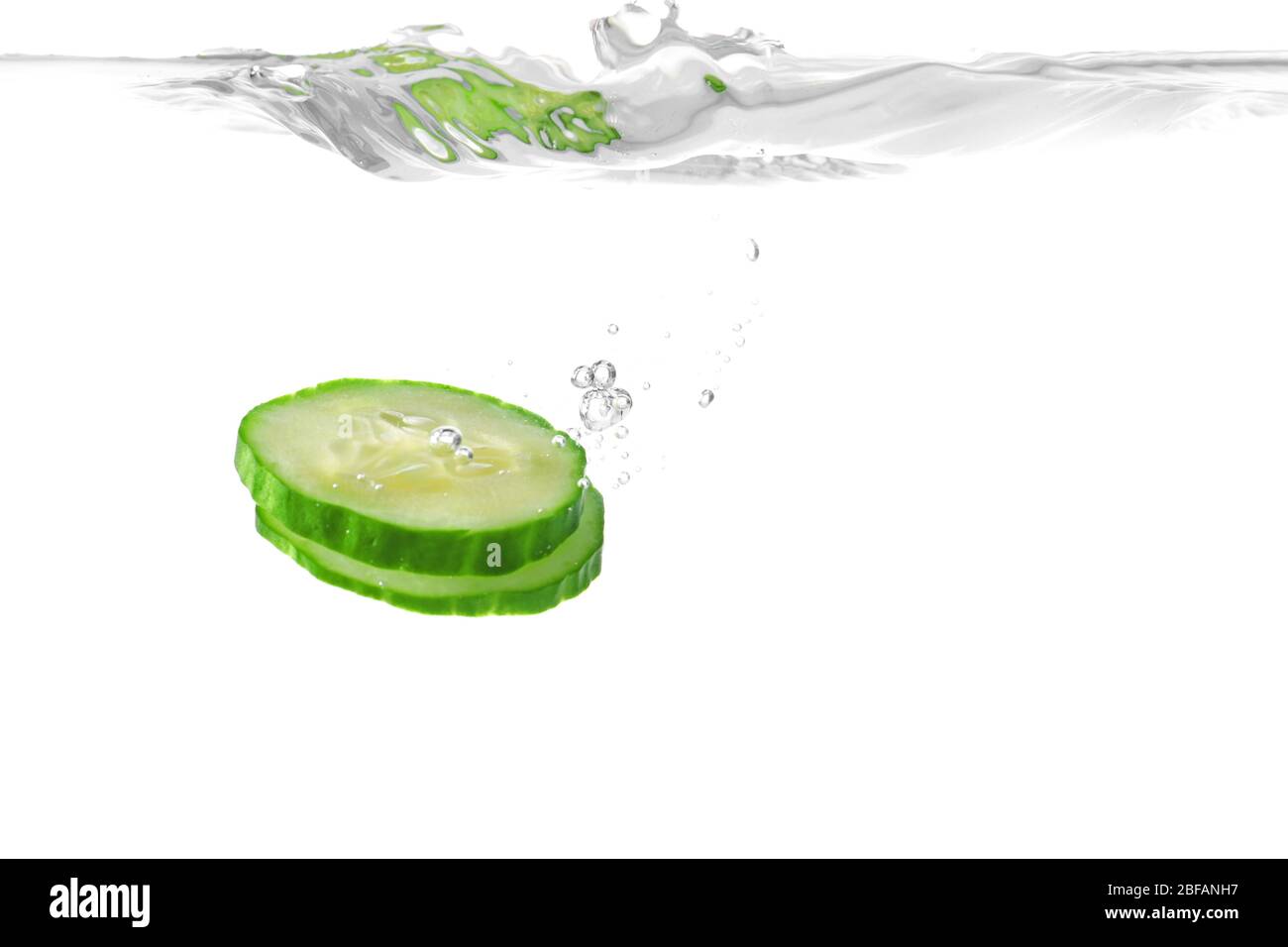 Chute de tranches de concombre frais dans l'eau sur fond blanc Banque D'Images