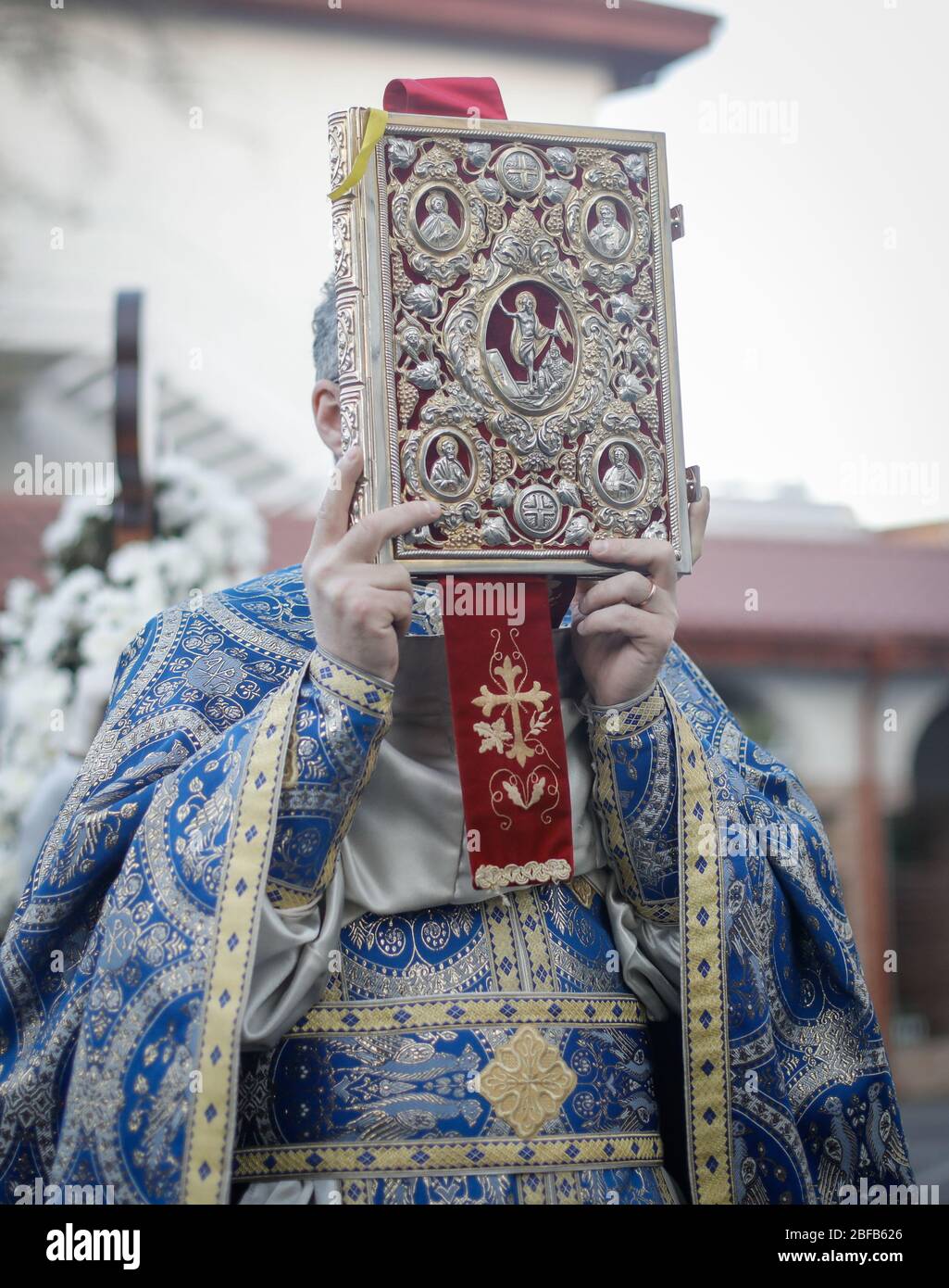 Profondeur de champ peu profonde (foyer sélectif) avec un prêtre chrétien orthodoxe roumain tenant une Sainte Bible en dehors d'une église. Banque D'Images
