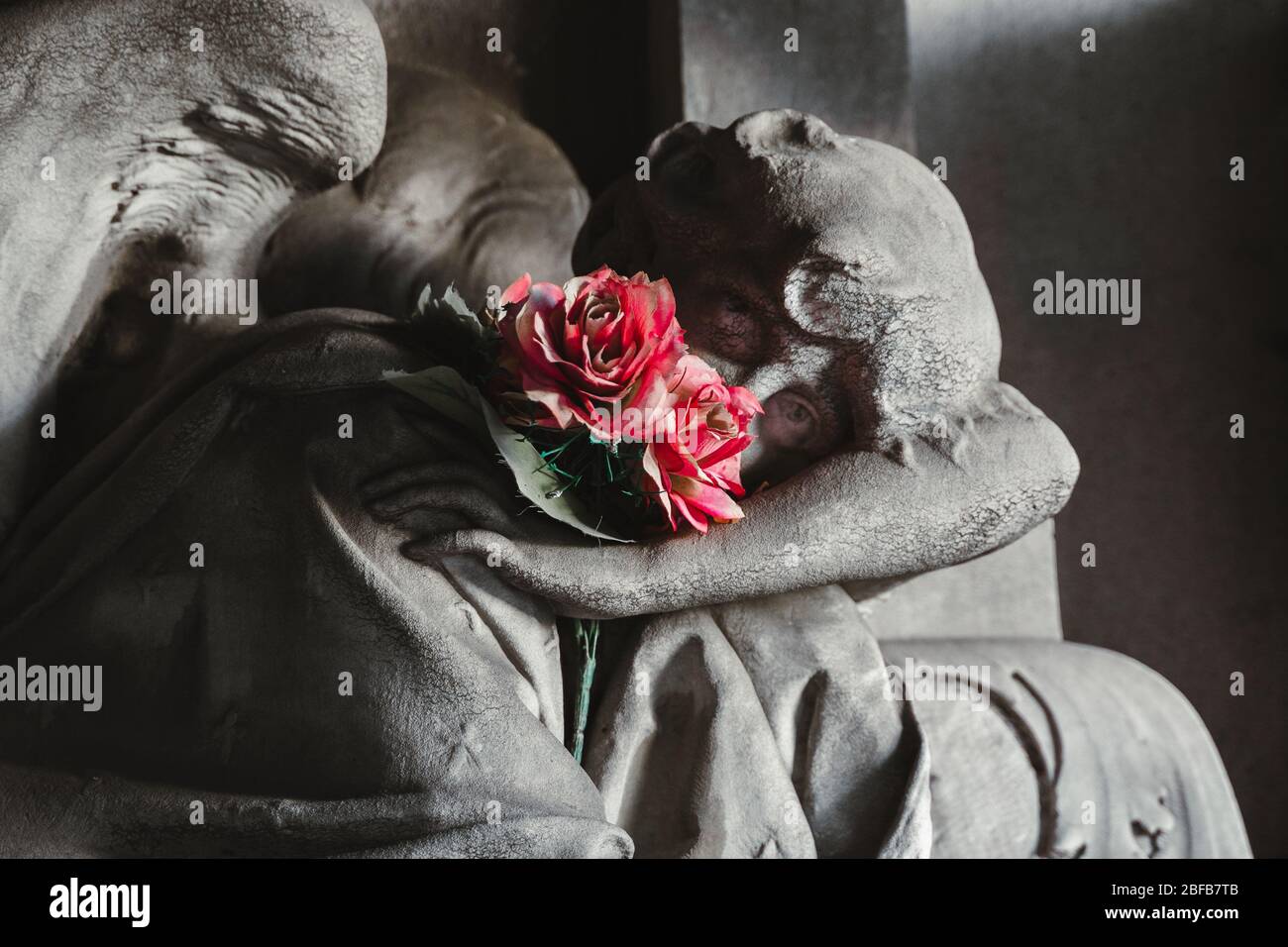 sculpture d'ange de granit de pierre avec fleurs sur pierre de tête dans un vieux cimetière. ange lapié noir et blanc pleurant sur les funérailles. Cimetière ancien Banque D'Images