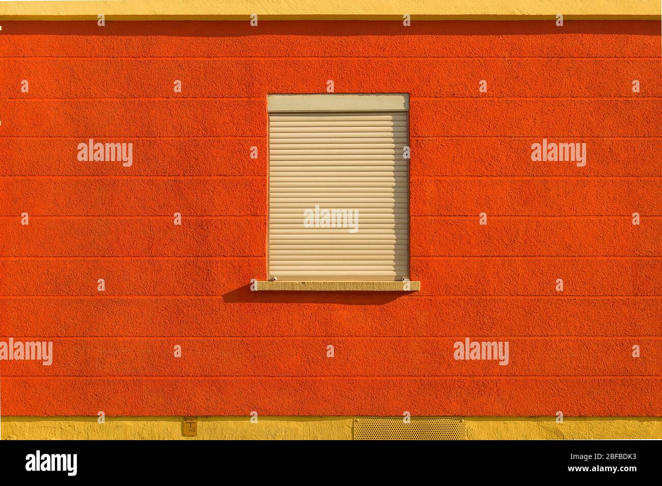 Façade aux couleurs vives rouge orange jaune socle une fenêtre se stores au milieu d'un motif horizontal Banque D'Images