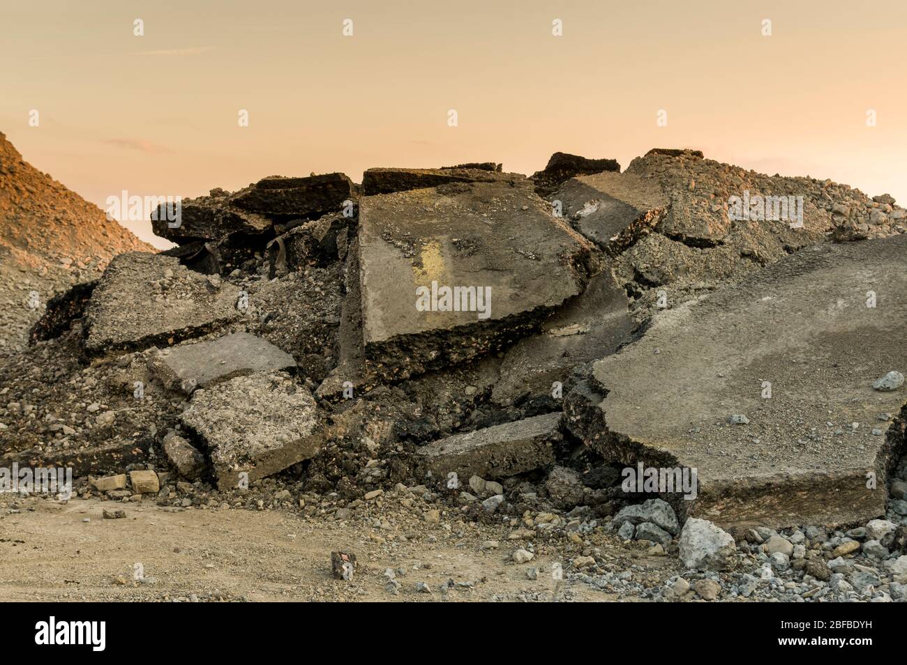 Décombres sur un chantier routier, asphalte brisé et morceaux de bitume d'une surface de route à partir de la démolition d'une route au coucher du soleil Banque D'Images