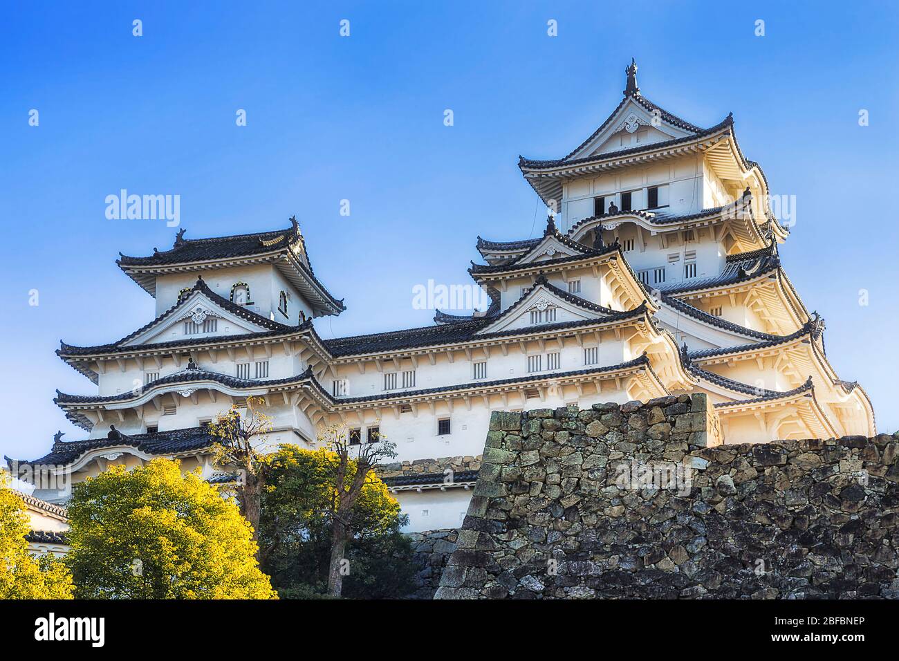 Murs blancs et tours du château traditionnel japonais historique à Himeji sur des murs massifs de pierre contre le ciel bleu. Banque D'Images