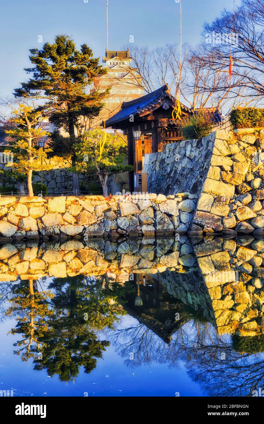 Murs en pierre autour du parc historique de la ville d'Himeji au Japon au lever du soleil avec une grande tour blanche qui se reflète dans les eaux de la lune. Banque D'Images