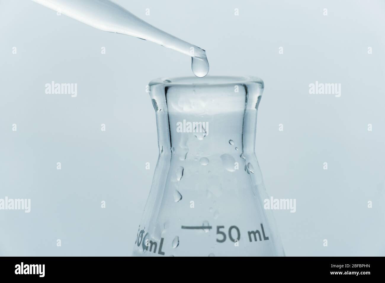 fermer la goutte d'eau claire propre dans la fiole en verre dans le fond bleu du laboratoire de recherche médicale Banque D'Images