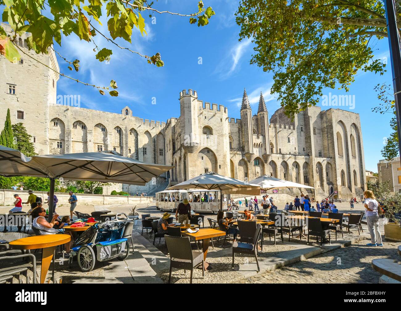 Les touristes peuvent prendre un repas dans un café-terrasse situé en face du Palais médiéval du Pape dans la région de Provence d'Avignon France en tant que tramway touristique à proximité Banque D'Images