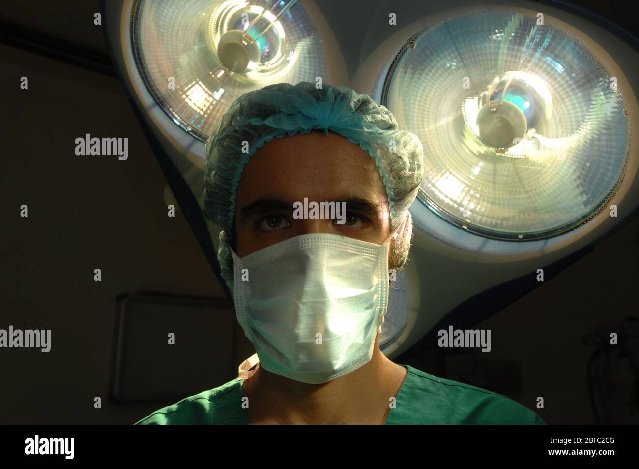 Un chirurgien masqué se trouve sous un ensemble de lampes de théâtre d'opération Banque D'Images