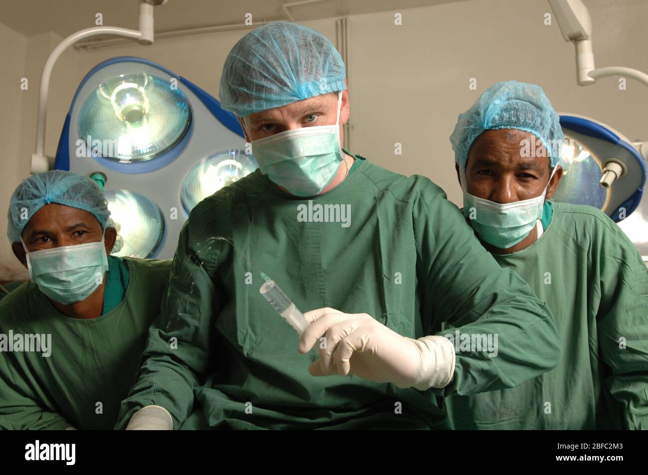 Chirurgien assis à côté de deux assistants, tenant une seringue hypodermique Banque D'Images