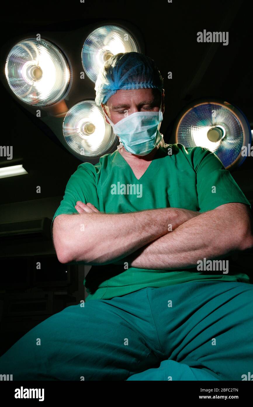 Un chirurgien fatigué est assis sur une table d'opération avec des bras repliés Banque D'Images