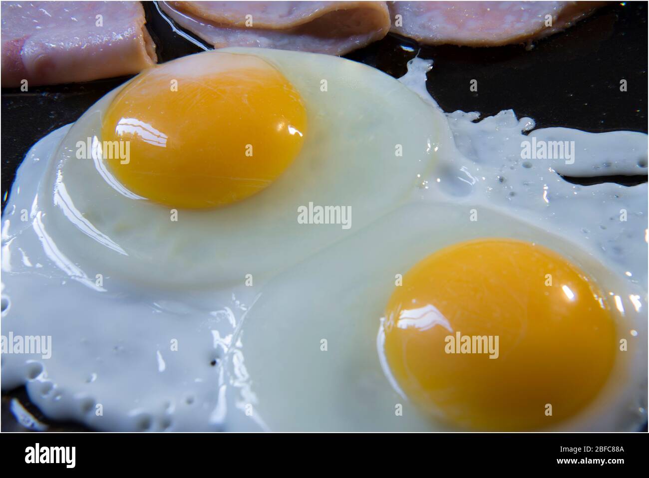 Gros plan ou macro-photographie de la préparation d'œufs et de jambon trop faciles, sur une casserole de cuisine dans le cadre d'un petit déjeuner classique. Cuisson des œufs sur une poêle Banque D'Images