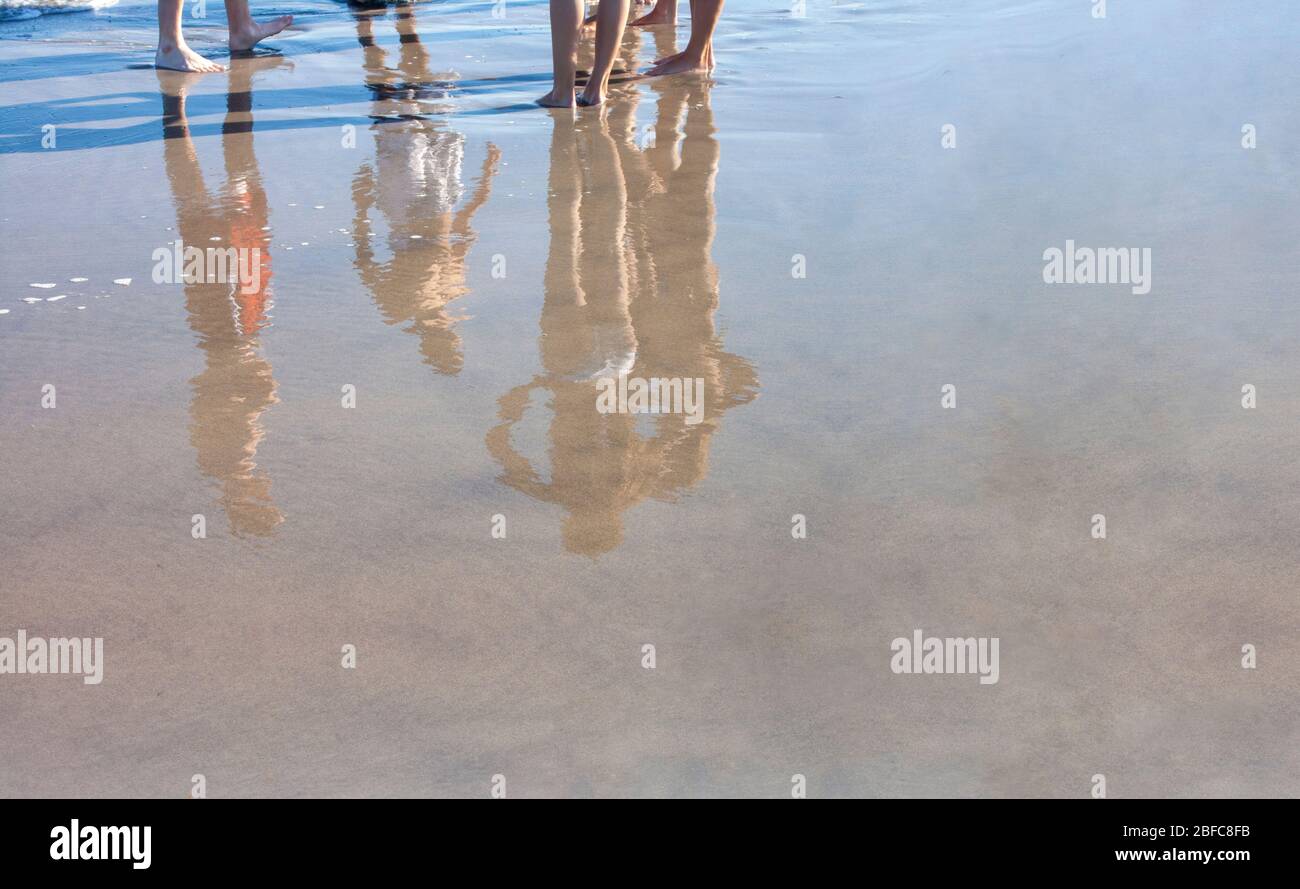 jeunes couples de plage se tenant dans les bains sur la rive humide avec des réflexions de sable humide Banque D'Images