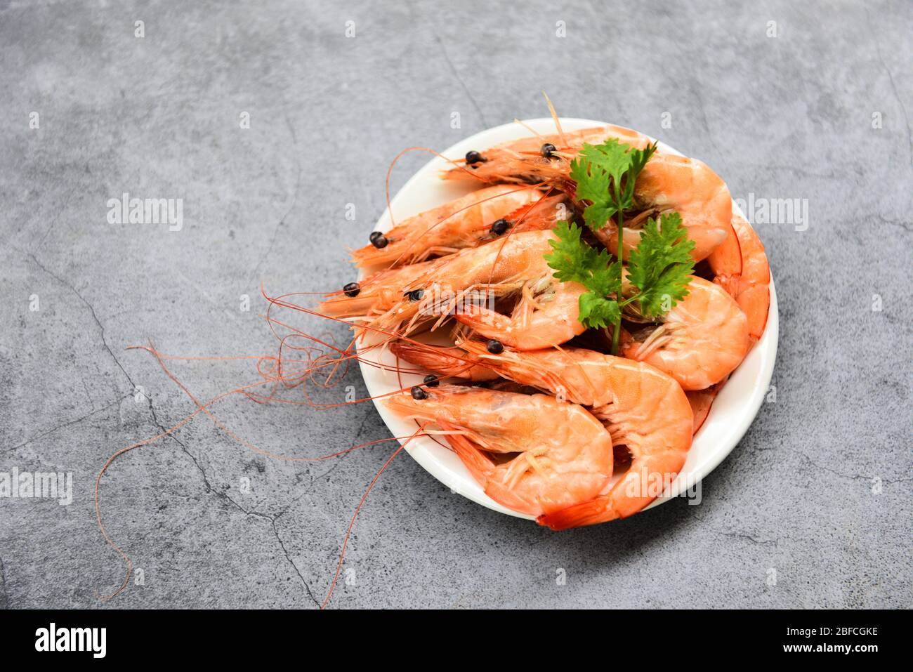 crevettes fraîches sur la plaque blanche avec ingrédients coriandre aux herbes / cuisson des crevettes aux fruits de mer servies sur fond de table gris Banque D'Images