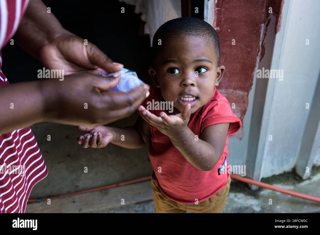 Un enfant de deux ans atteint pour assainisseur des mains dans la commune de Hout Bay à Imizamo Yethu, près du Cap, Afrique du Sud, pendant l'éclosion de COVID-19 Banque D'Images