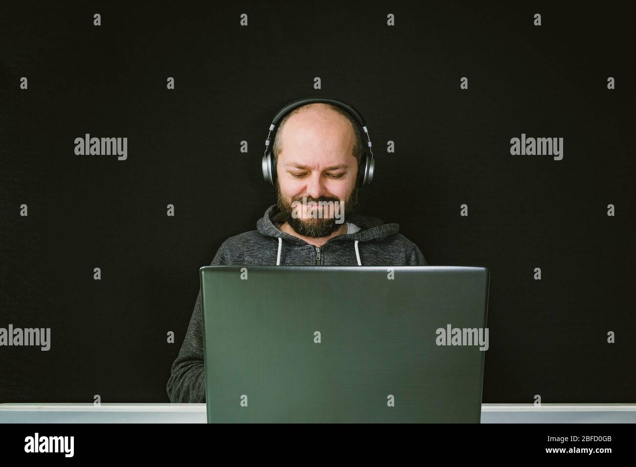 Homme à brancher et casque sur la tête assis derrière l'ordinateur portable, confus, infructueux, fond noir Banque D'Images