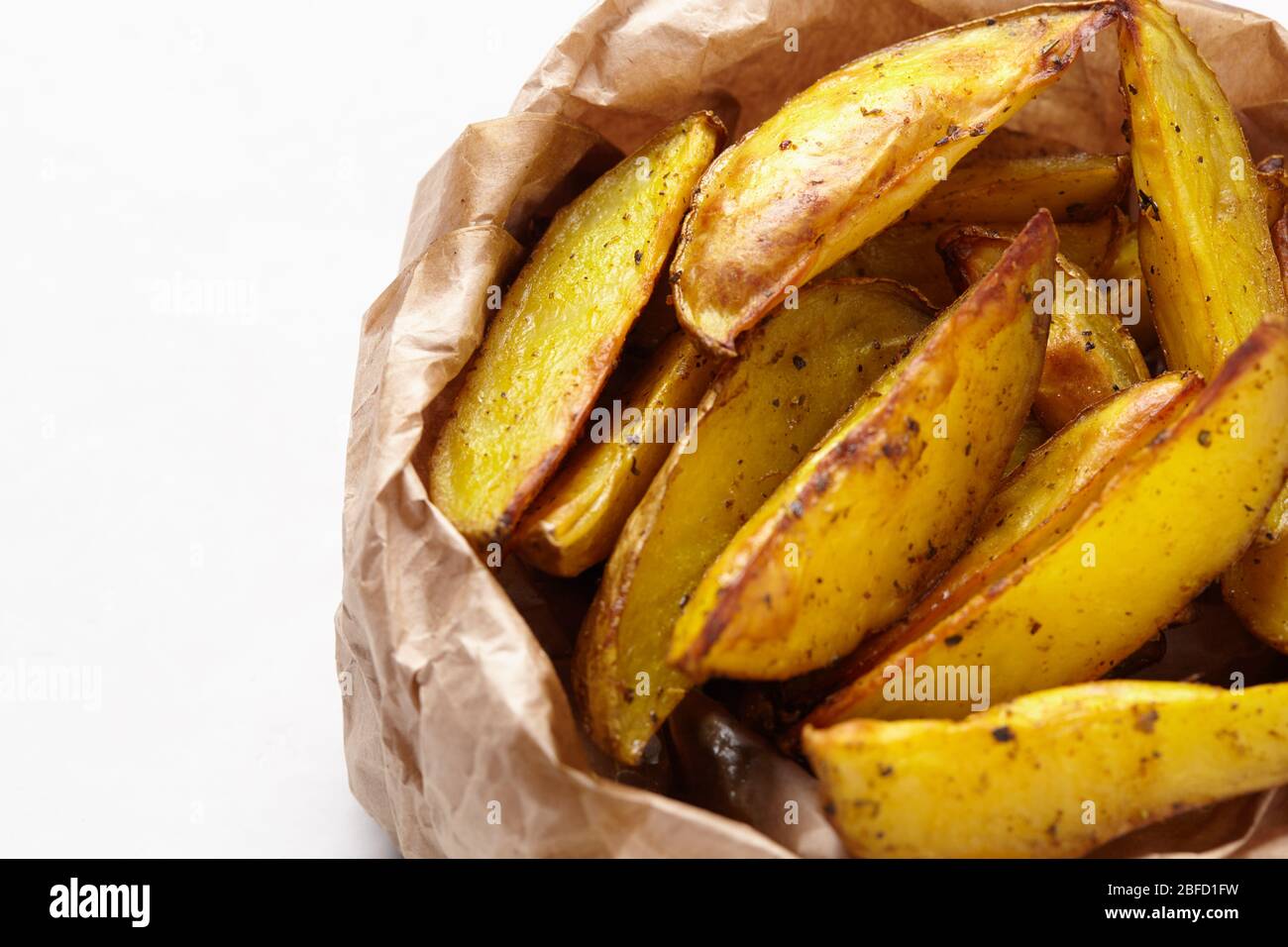 Tranches de frites maison dans un sac en papier marron sur fond blanc. Pommes de terre frites. Banque D'Images