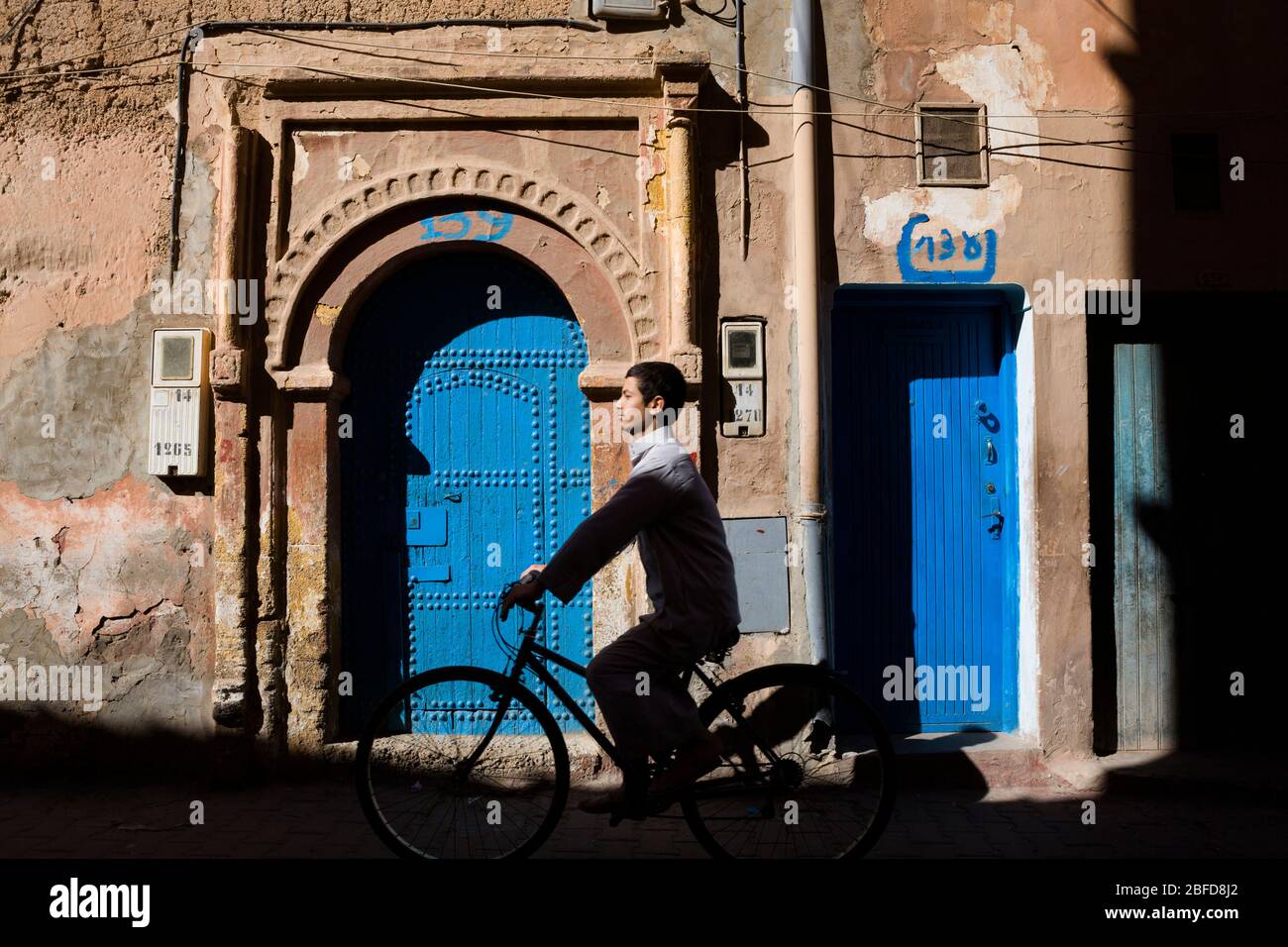 Cycliste local passant par une porte turquoise décorée dans le Sahara occidental, au Maroc. Banque D'Images