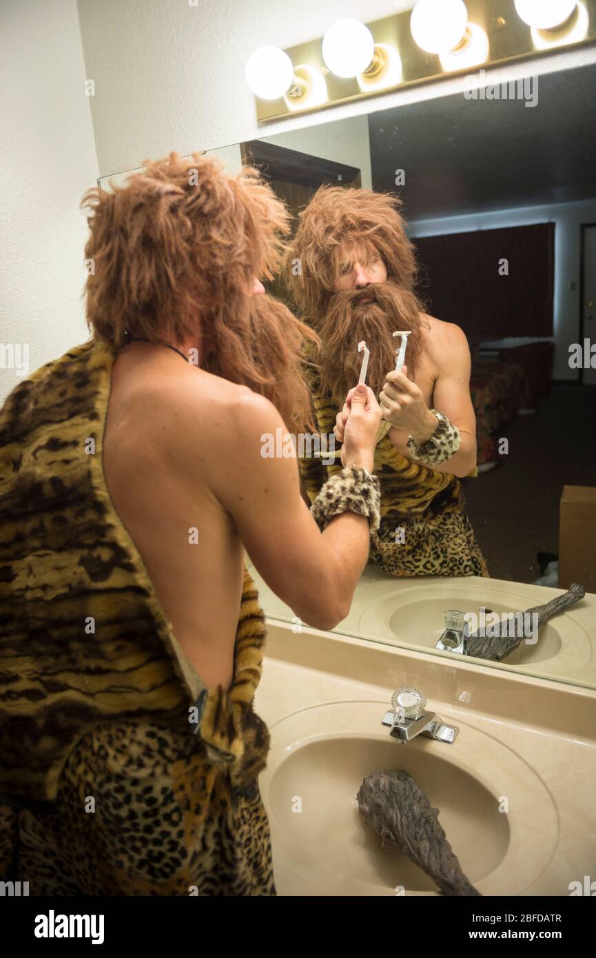 Il y avait un caveeman confus avec des cheveux trop grands et une barbe qui tenait un rasoir devant le miroir à l'évier de la salle de bains Banque D'Images