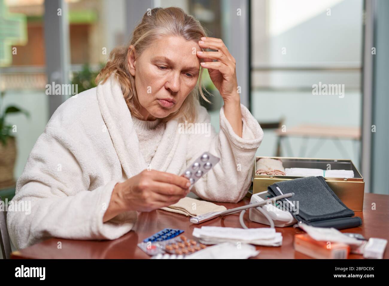 Portrait d'une femme atteinte de maturité et troublée assise à la maison et listant la description des médicaments dans sa main Banque D'Images