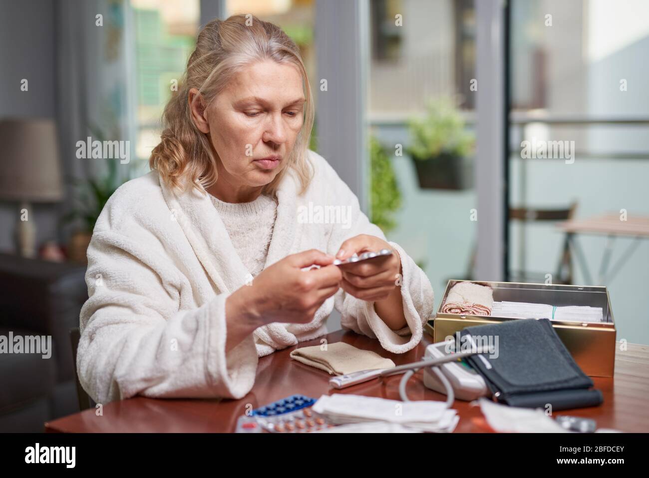 Portrait d'une femme atteinte de maturité et troublée assise à la maison et listant la description des médicaments dans sa main Banque D'Images