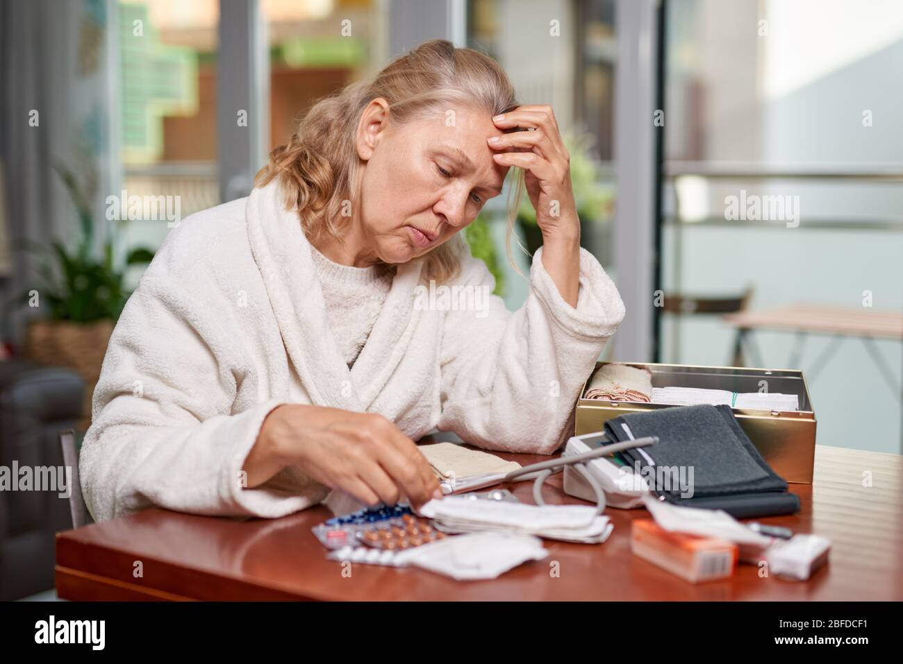 Portrait d'une femme atteinte de maturité et troublée assise à la maison et listant la description des médicaments dans sa main Banque D'Images