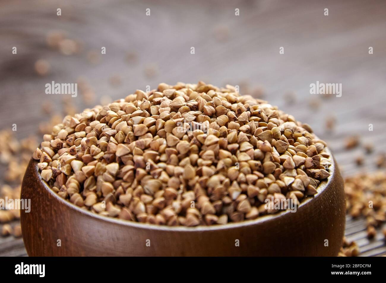 Gruaux de sarrasin (graines décortiquées) dans un bol en bois, foyer sélectif. Grains entiers de sarrasin sur table brune, gros plan. Super-nourriture, nourriture saine sans gluten Banque D'Images