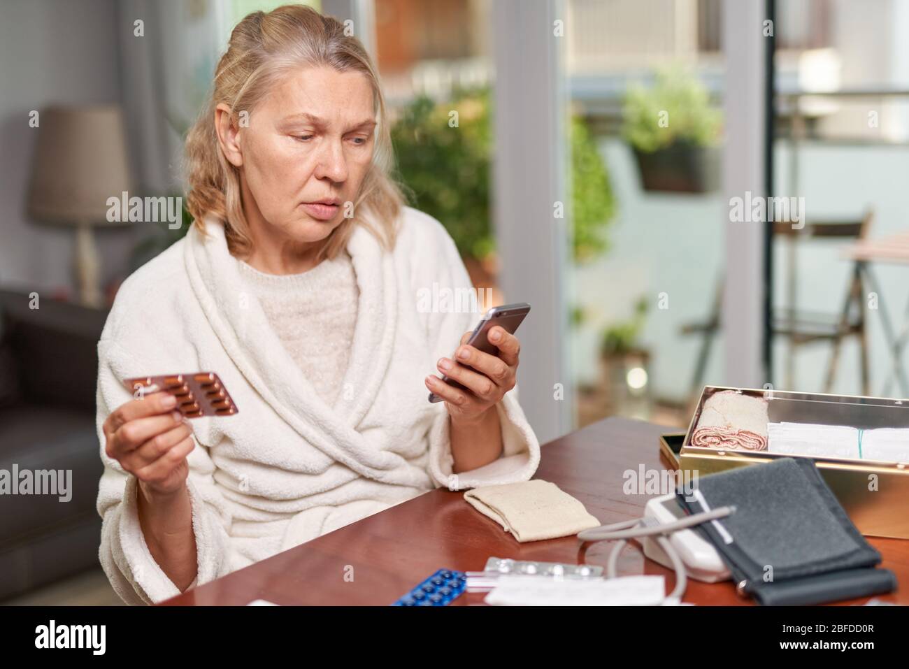 Portrait d'une femme atteinte de maturité et en difficulté assise à la maison et tenant un téléphone et des tablettes Banque D'Images