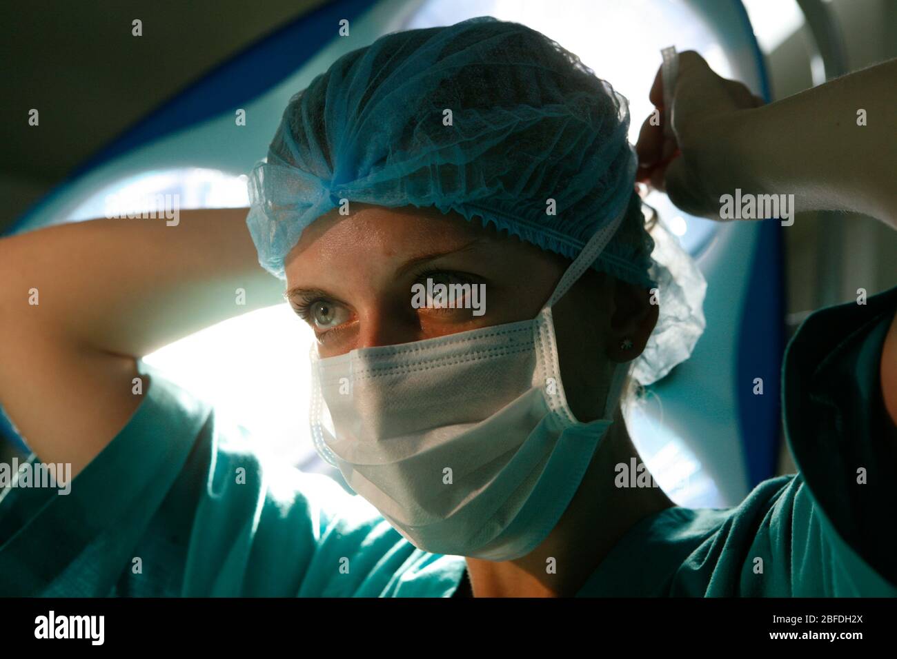 Une chirurgien féminin lie son masque chirurgical autour de son visage sous les lumières du théâtre Banque D'Images