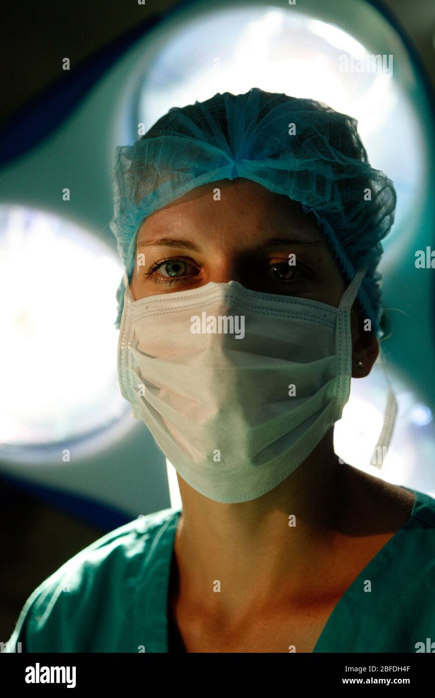 Un chirurgien féminin regarde directement la caméra de dessous les lumières chirurgicales Banque D'Images
