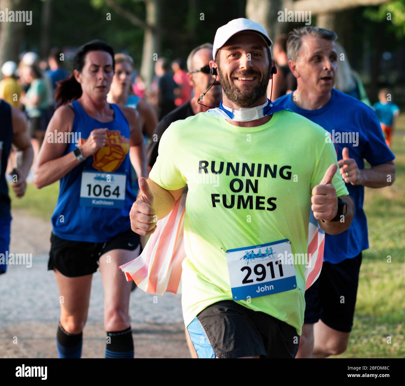 North Babylone, New York, USA - 8 juillet 2019: Coureur de course A 5 K à un parc d'État donne deux pouces vers le haut et porte un cap pendant la course. Banque D'Images