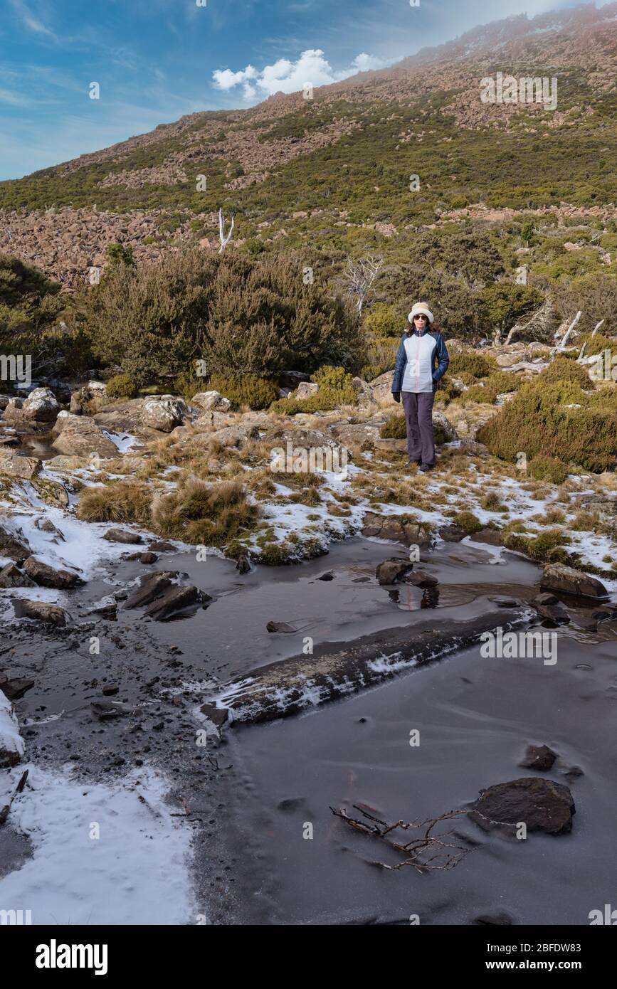 Portrait d'une femme en randonnée dans des vêtements d'hiver debout à côté d'un trou d'eau surgelé dans la haute campagne sur la pente de montagne Ben Lomond en Tasmanie. Banque D'Images