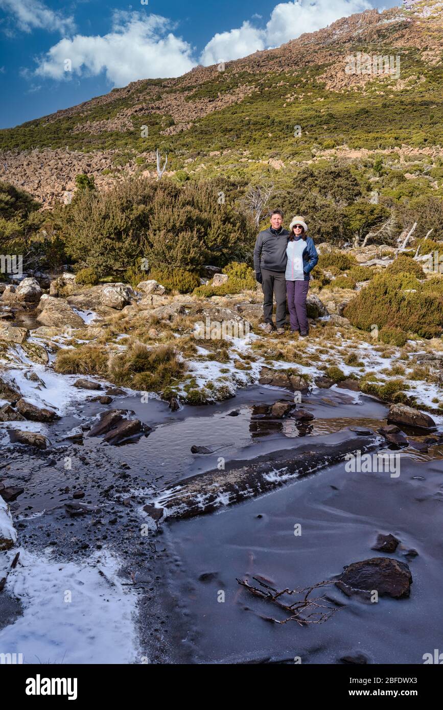 Portrait de couple de randonnée en vêtements d'hiver debout à côté d'un trou d'eau surgelé sur la pente de montagne Ben Lomond en Tasmanie. Banque D'Images