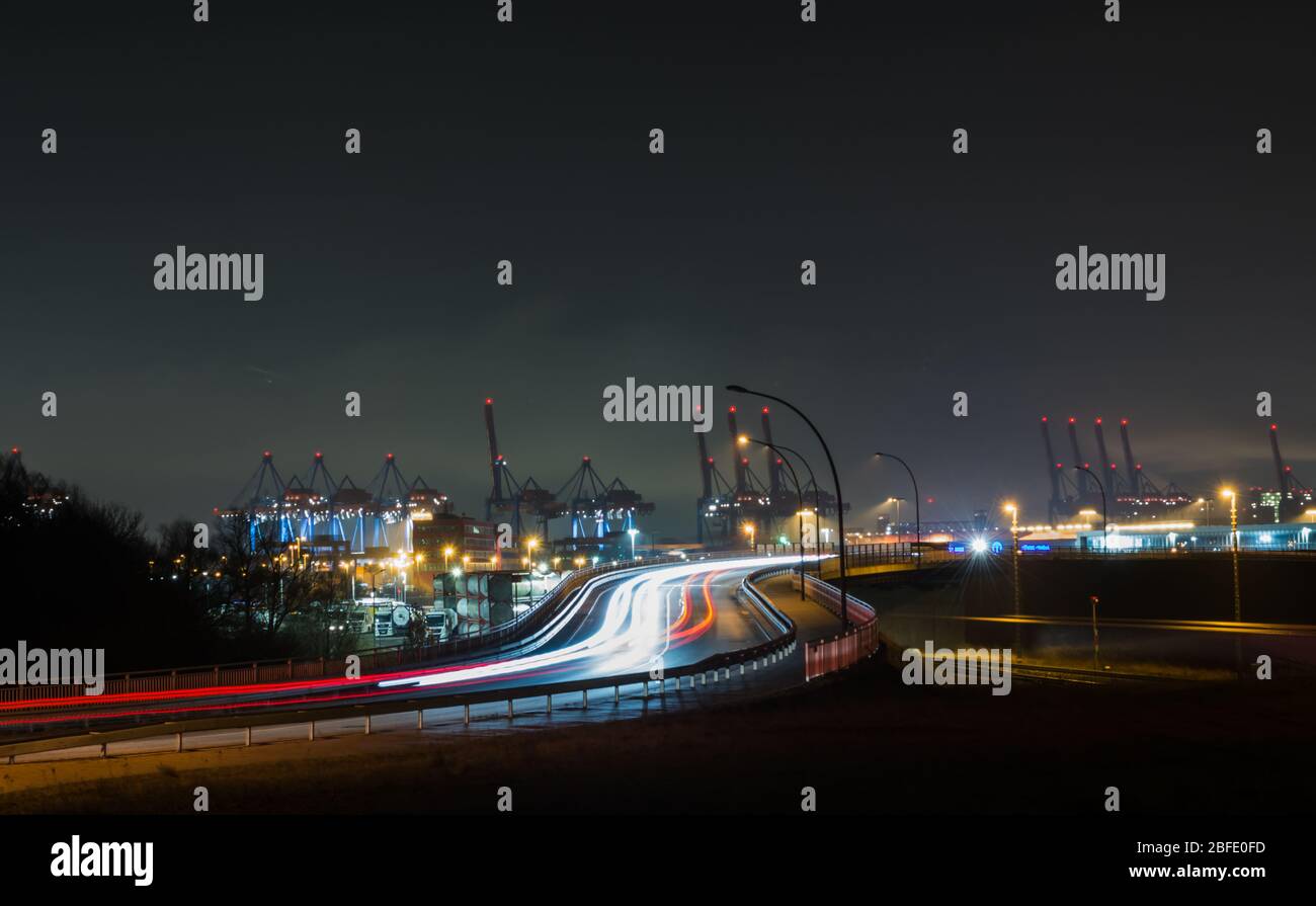 Exposition prolongée prise de vue de nuit sur la voie automobile et les faisceaux lumineux des voitures qui passent par le port industriel et la zone portuaire de Hamb Banque D'Images
