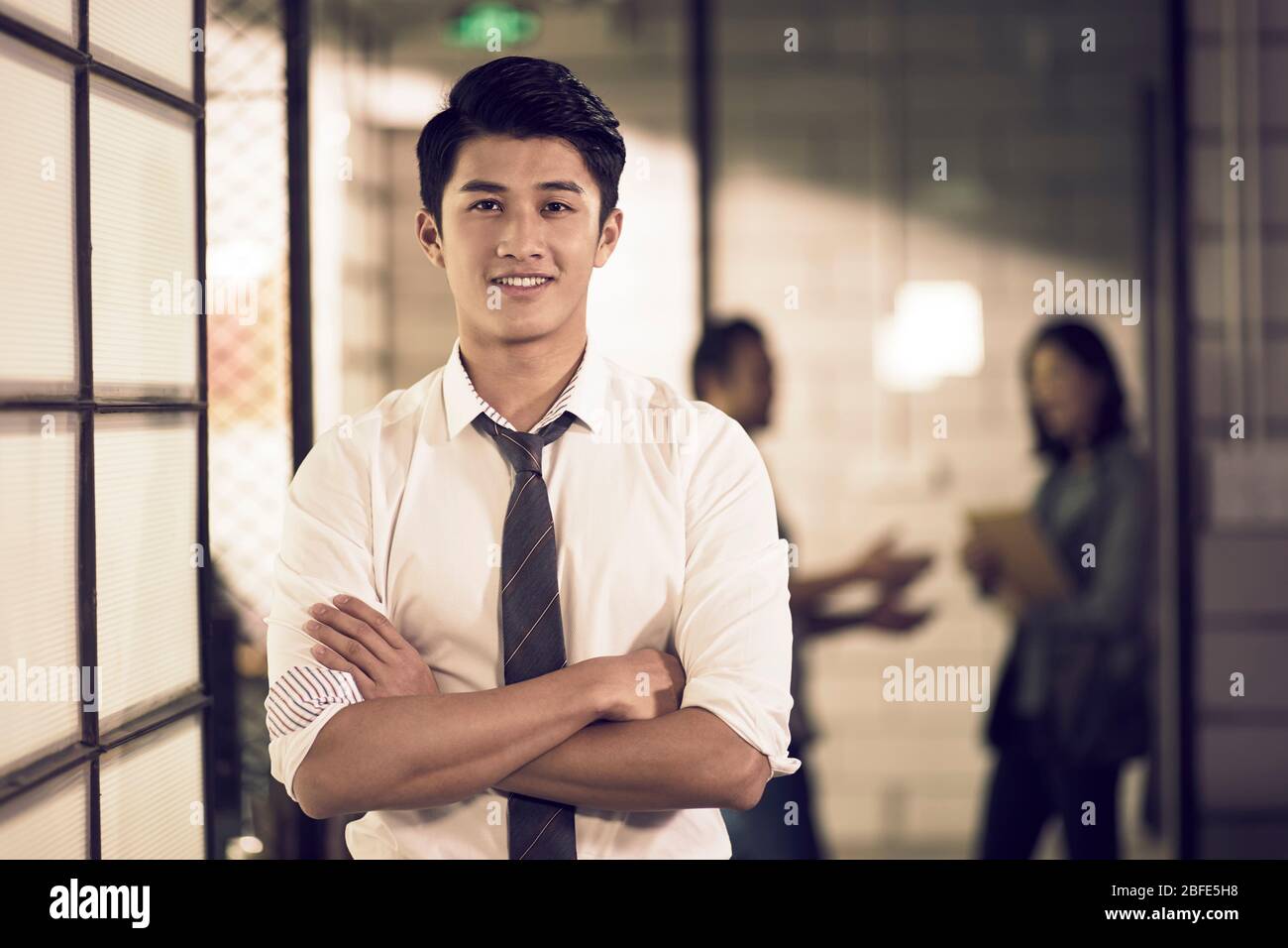portrait d'un jeune entrepreneur asiatique prospère confiant debout dans les bras de bureau croisé Banque D'Images