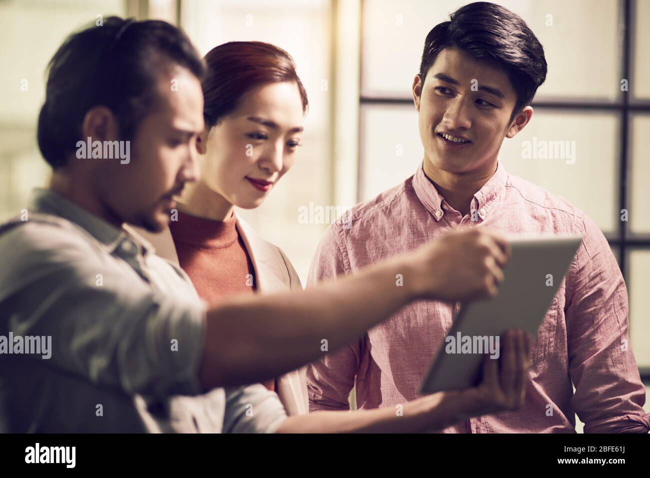 trois jeunes entrepreneurs asiatiques travaillant ensemble au bureau à la recherche d'une tablette numérique Banque D'Images