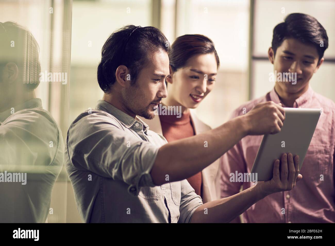 trois jeunes entrepreneurs asiatiques travaillant ensemble au bureau à la recherche d'une tablette numérique Banque D'Images