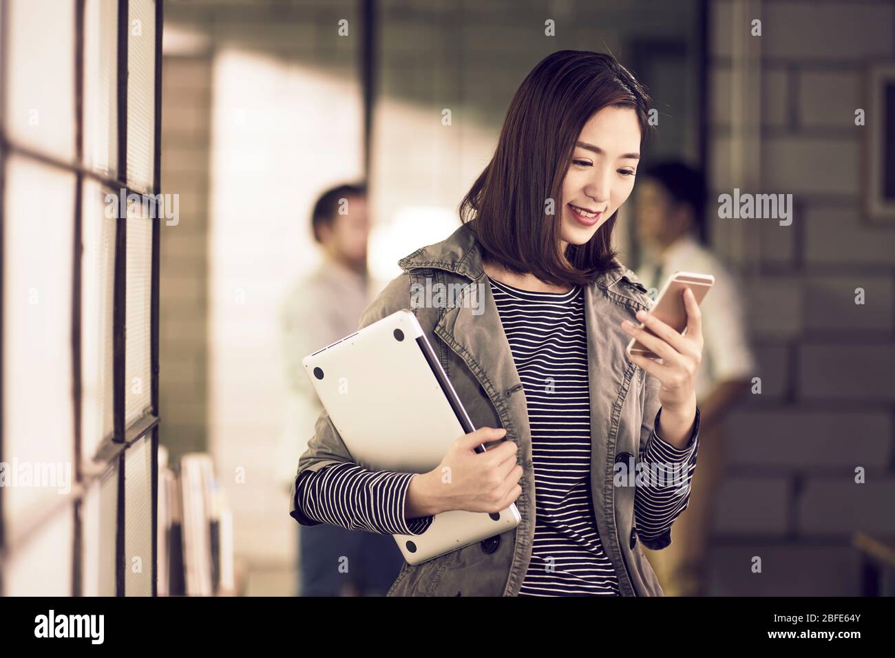 jeune entrepreneur asiatique de femme d'affaires tenant un ordinateur portable regardant le téléphone portable souriant Banque D'Images