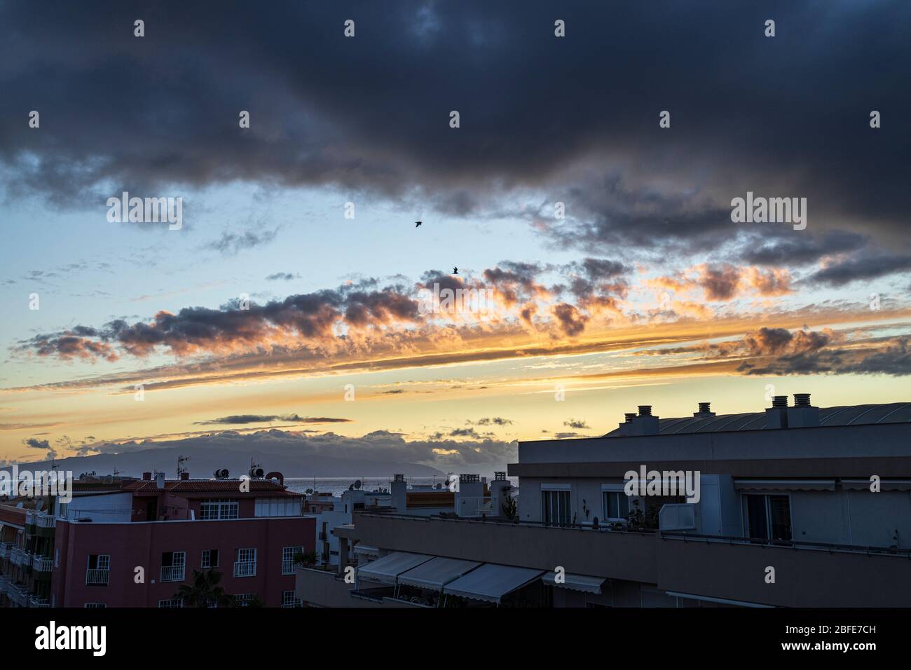 Quelques oiseaux survolent le village en face d'un ciel coloré au coucher du soleil, Playa San Juan, Tenerife, îles Canaries, Espagne Banque D'Images