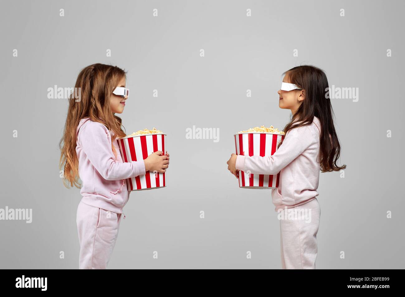 deux belles petites filles blanches souriantes dans des verres tridimensionnels rouges qui tiennent des seaux à maïs soufflé et se regardaient les unes les autres Banque D'Images