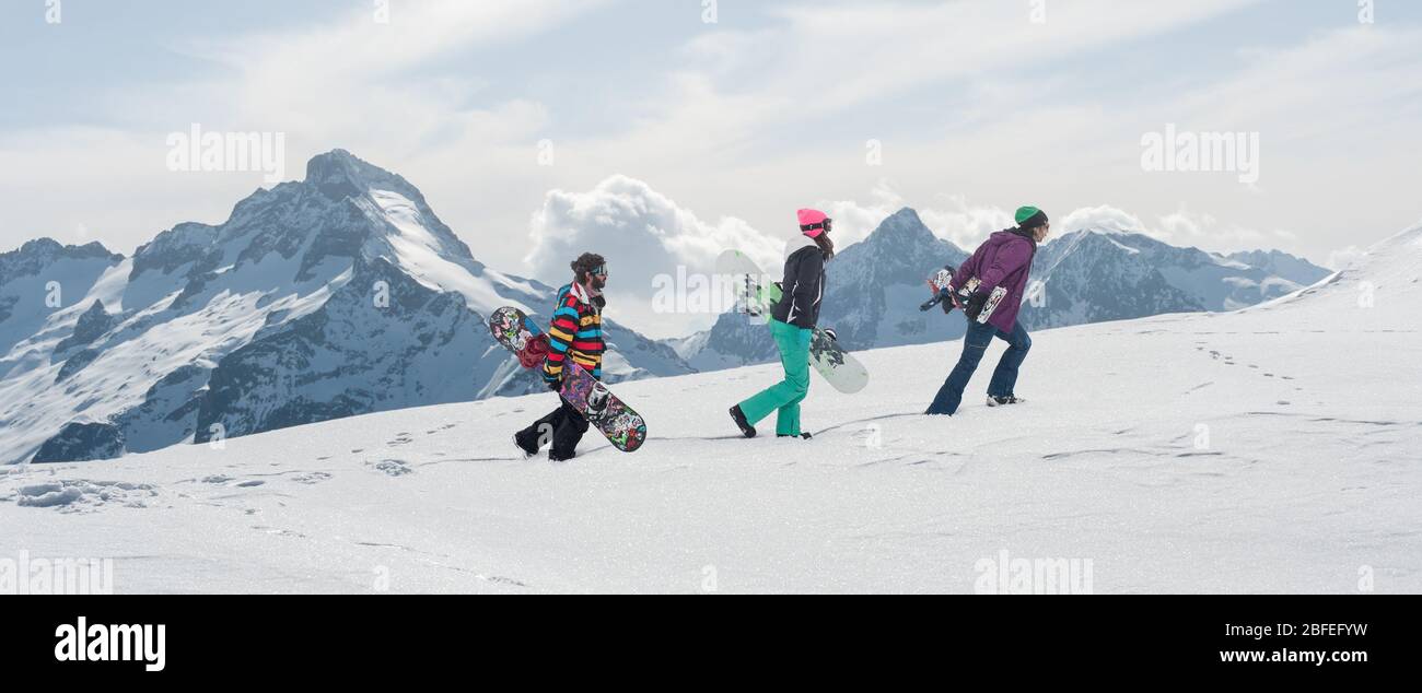 Groupe de trois surfeurs de neige freeride rouleaux et promenades planche à neige sur la piste de neige, et profiter dans la magnifique chaîne de montagnes des Alpes en arrière-plan. Bac Banque D'Images