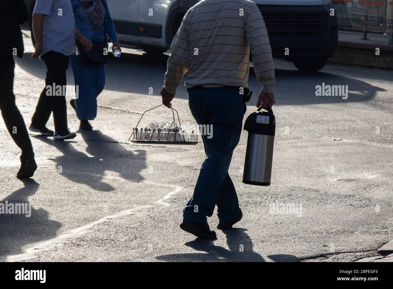 Homme vendant du thé dans des thermos dans la rue. D'autre part, il porte des verres en verre sur un plateau de poignée Banque D'Images