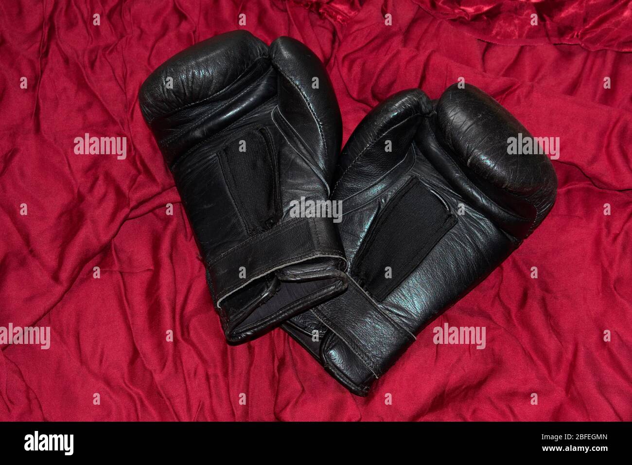 Une paire de gants de boxe en cuir noir que je menais sur satin rouge. Banque D'Images