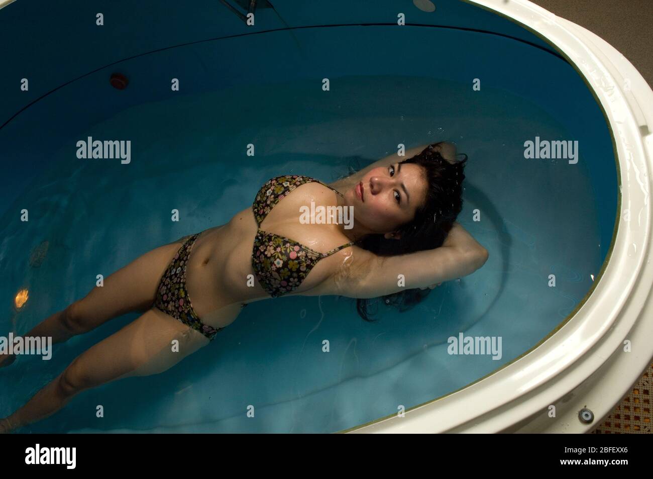 Une jeune femme se trouve dans un réservoir de flottaison relaxant rempli d'eau et de sels Epson. Banque D'Images