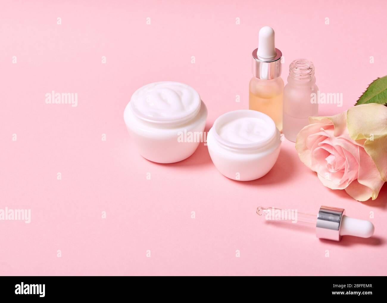 Concept anti-âge. Crème faciale acide hyaluronique et rose isolée sur rose gros plan de l'espace de copie Banque D'Images