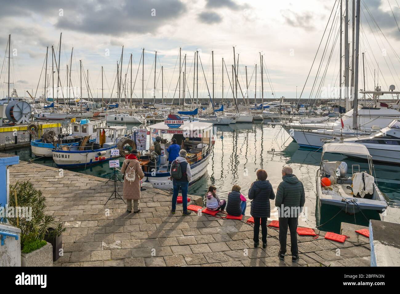 Vue sur le port avec des gens en ligne pour acheter du poisson frit à partir d'un bateau de pêche 'friggitoria' amarré au quai, Sanremo, Ligurie, Italie Banque D'Images