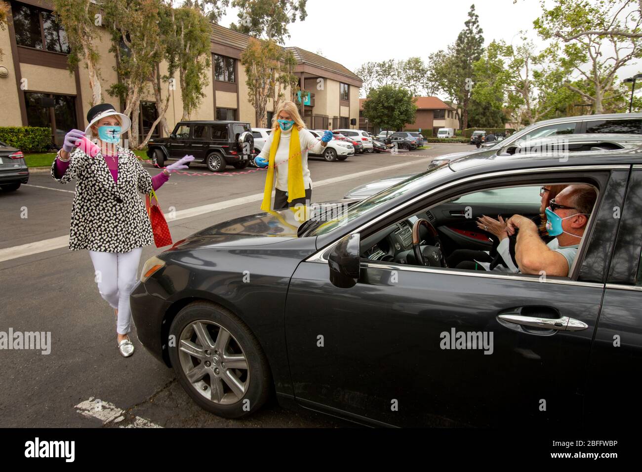 Les bénévoles portent un masque de sécurité en raison de l'éclosion de coronavirus ou de COVID-19 lorsqu'ils décorent des voitures arrivant avec des rubans dans un service de Pâques en voiture dans un parc de bureaux de Santa Ana, Californie. Banque D'Images