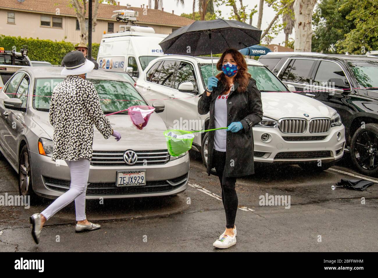 Lors d'un service de Pâques en voiture dans un parc de bureaux de Santa Ana, Californie, des bénévoles en masques de sécurité et gants en caoutchouc recueillent des demandes de prière des fidèles dans leur voiture à l'aide d'un filet à long manche. Le service de drive-in a été provoqué par l'éclosion de coronavirus ou COVID-19 Banque D'Images