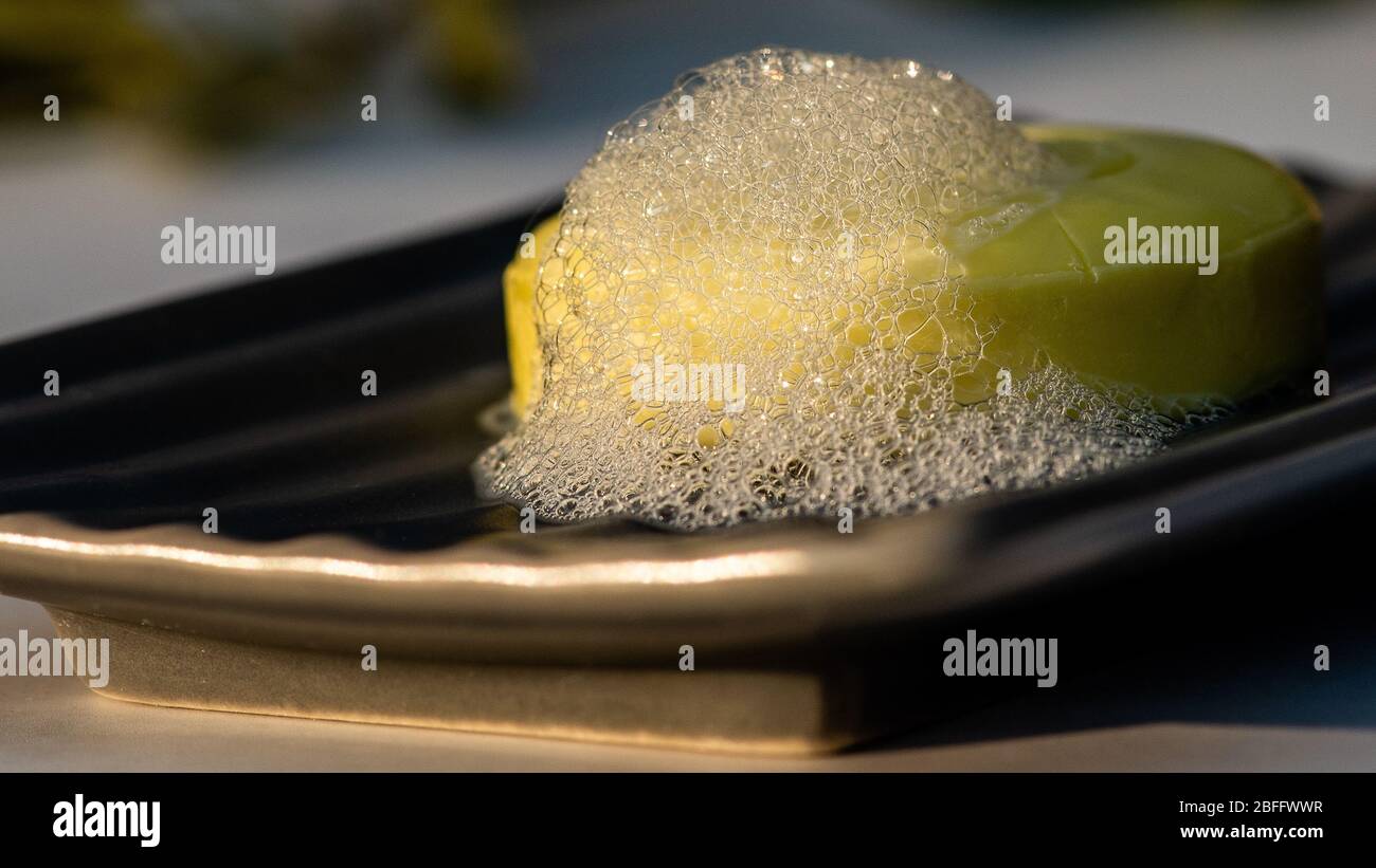 Savon à main d'huile d'olive dans un plat en céramique gris avec bulles de lather et feuilles de branches d'olive décoration Banque D'Images