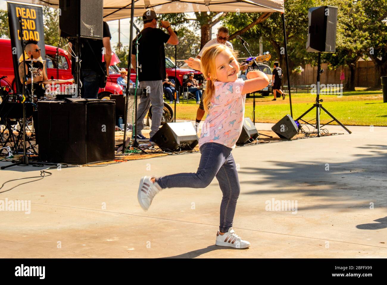 Une jeune fille de trois ans danse avec enthousiasme à un groupe de rock lors d'une foire extérieure dans un parc Costa Mesa, Californie. Banque D'Images