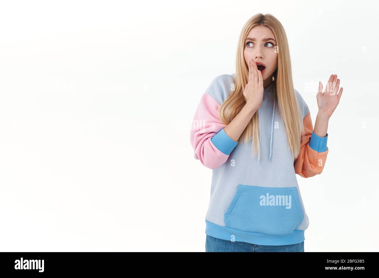 Fille blonde effrayée dans un élégant sweat à capuche, haletant, couvrir la bouche ouverte et regardant loin avec l'expression effrayée, se sentant inescure et terrifié de fort Banque D'Images